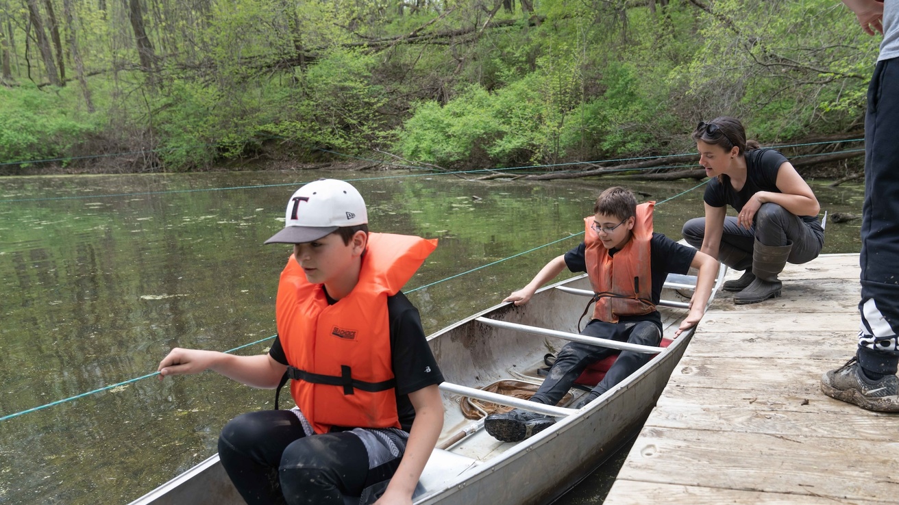 Woman helps boys into a canoe on a pond